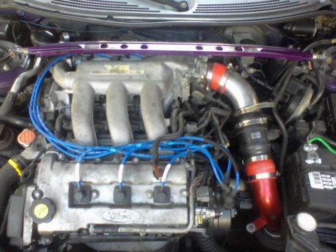 1995 Ford Probe - Close-up view of a Ford V6 engine bay with blue spark plug wires and a red intake pipe. A purple strut bar is visible across the top of the…