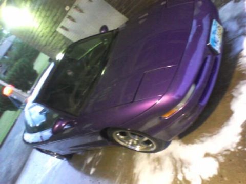 1995 Ford Probe - A low-angle, tilted shot of a purple 1995 Ford Probe with its headlights down, parked on a wet surface with suds. A license plate is visibl…
