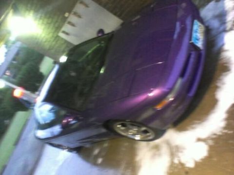 1995 Ford Probe - A low-angle, slightly tilted shot of a purple Ford Probe with its headlights down. The car is parked on a wet surface, possibly after being…