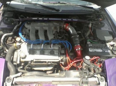1995 Ford Probe - The engine bay of a purple 1995 Ford Probe, nicknamed "Starscream", is shown with modifications including a red intake pipe and blue spark…
