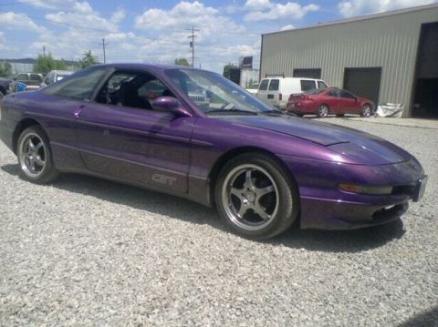 1995 Ford Probe - A purple 1995 Ford Probe GT is parked on a gravel lot in front of a metal building. The car is viewed from the side at a 3/4 front angle.