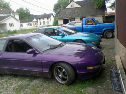 1995 Ford Probe - A purple Ford Probe GT is parked in front of a teal Ford Probe and a blue pickup truck. The purple car is in the foreground, showing its dr…