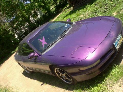 1995 Ford Probe - A purple 1995 Ford Probe is parked on a dirt path next to a grassy area with trees in the background. A pink "X" sticker is visible on the…