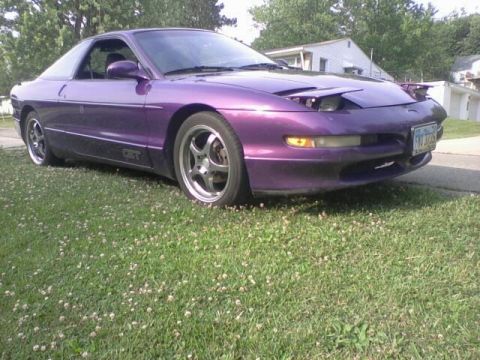 1995 Ford Probe - A low-angle shot of a purple Ford Probe GT parked on a grassy lawn with clover. The car's pop-up headlights are partially raised, revealing…