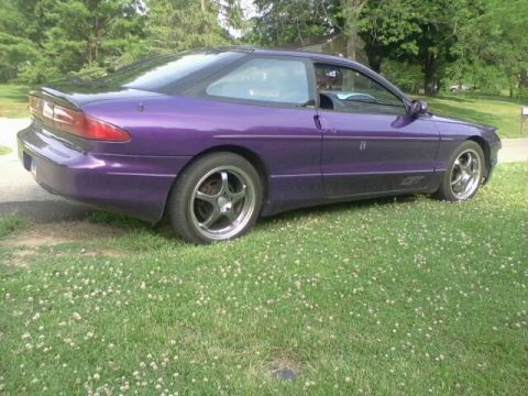 1995 Ford Probe - A purple 1995 Ford Probe GT is parked on a grassy lawn, viewed from the rear passenger side. The car features aftermarket wheels and a rear…