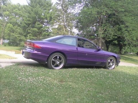 1995 Ford Probe - The side profile of a purple 1995 Ford Probe GT is shown parked on a grassy lawn with trees in the background. The car features aftermarket…