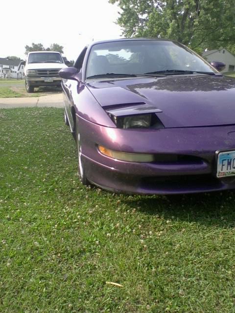 1995 Ford Probe - The front quarter panel of a purple 1995 Ford Probe is visible, parked on a grassy lawn. A white pickup truck is parked in the background.