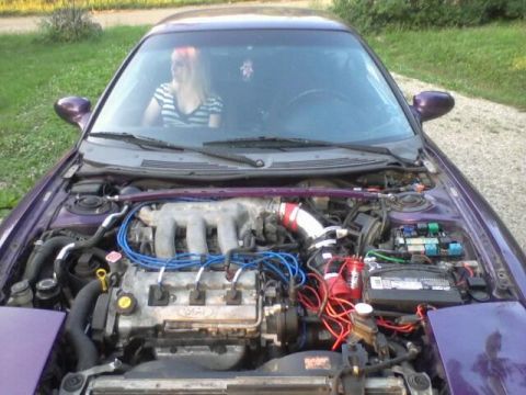 1995 Ford Probe - The open hood of a purple 1995 Ford Probe reveals its engine bay, with a woman visible through the windshield. The engine features blue spa…