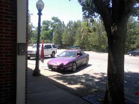 1995 Ford Probe - A purple 1995 Ford Probe is parked on a paved lot next to a sidewalk. A white SUV is parked behind it.