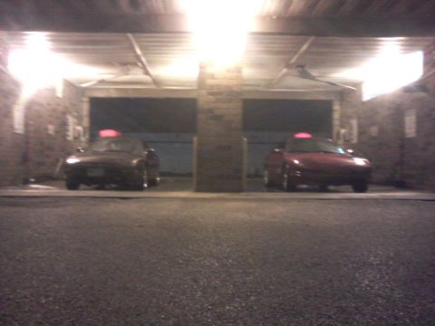1995 Ford Probe - Two red sports cars are parked side-by-side in a dimly lit garage. Both cars have a red light on their roofs.