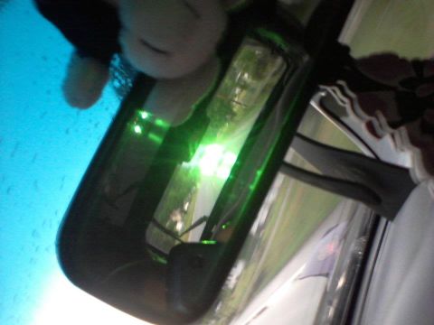 1995 Ford Probe - A reflection in a car's rearview mirror shows a plush toy and the bright green reflection of a light source. The exterior scene reflected i…