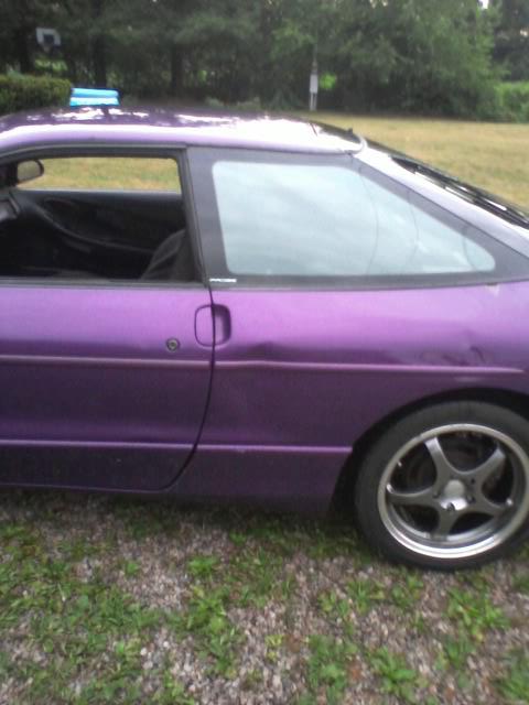 1995 Ford Probe - The side view of a purple 1995 Ford Probe shows its coupe body style, custom wheels, and a dent on the rear passenger door. A blue rack is…