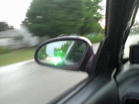 1995 Ford Probe - View from inside a car looking at the driver's side mirror, reflecting a green light and other vehicles on a road. The exterior of the car…