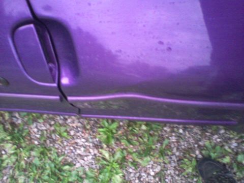 1995 Ford Probe - A close-up side view of a purple car door with a visible door handle and a slight dent. The lower part of the door is visible above a grave…