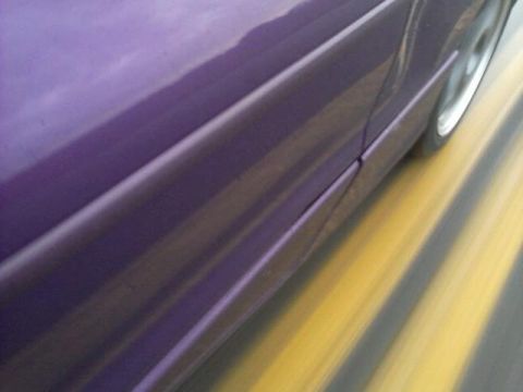 1995 Ford Probe - A close-up, motion-blurred side view of a purple car driving on a road with yellow and gray stripes. The car's body panels and a portion of…