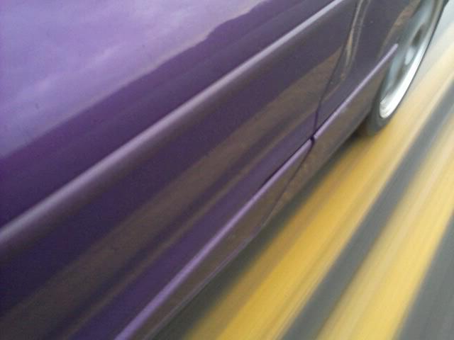 Purple car side view, motion blurred, with yellow and gray road stripes.