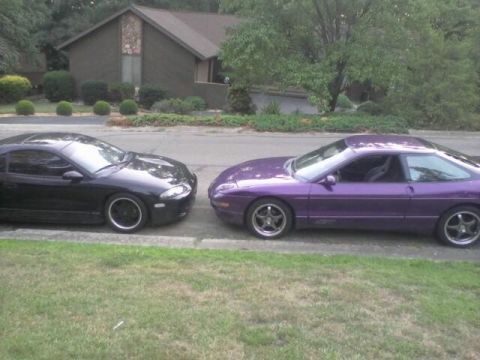 1995 Ford Probe - Two sports coupes, a black Mitsubishi Eclipse and a purple Ford Probe, are parked side-by-side on a paved surface in front of a residential…