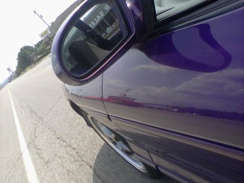 1995 Ford Probe - Side view of a purple car driving on a road, with reflections in the side mirror.
