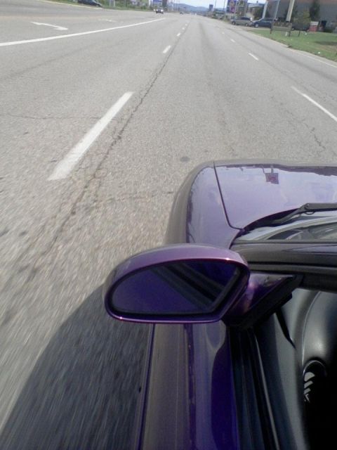 1995 Ford Probe - View from inside a purple car as it travels down a highway, showing the side mirror and part of the hood.