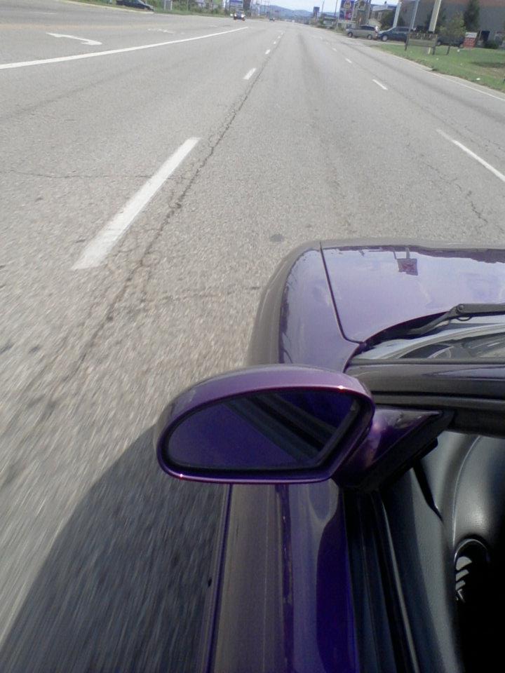 Purple car's side mirror and hood seen from driver's perspective on a highway