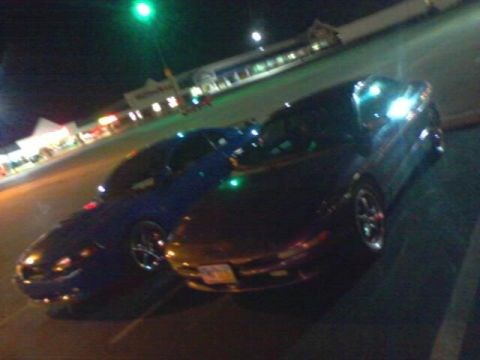 1995 Ford Probe - Two sports cars are parked side-by-side in a parking lot at night, with a store's lights illuminating the background.
