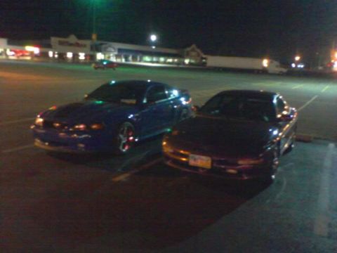 1995 Ford Probe - Two cars are parked in a dimly lit parking lot at night, with a store in the background.