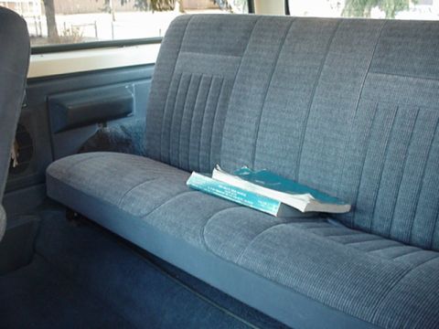 1993 Ford Bronco - The interior of a vehicle shows a blue upholstered back seat with two books resting on it.