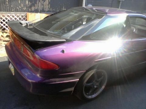 1995 Ford Probe - A purple sports coupe with a spoiler is parked outdoors, with sunlight glinting off its surface.