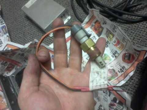 1995 Ford Probe - A hand holds a temperature sensor with attached wiring, with newspaper ads and a metal box in the background.