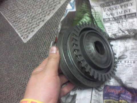 1995 Ford Probe - A hand holds a metal pulley and gear assembly, possibly automotive, over a newspaper.