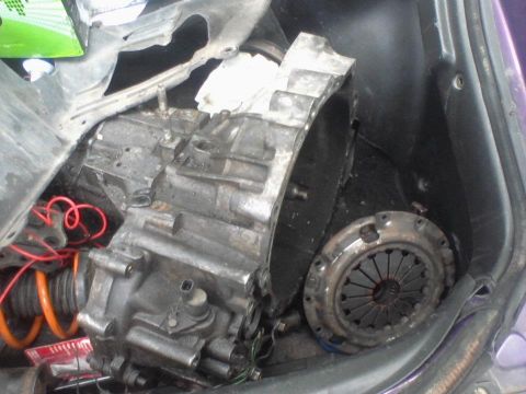 1995 Ford Probe - A disassembled car transmission and clutch assembly are visible in the trunk of a car. The transmission is grey and greasy, with red wiring…