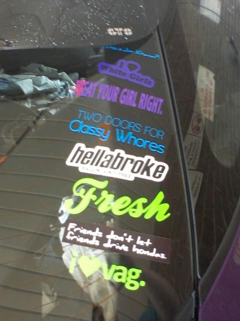 1995 Ford Probe - A close-up view of several colorful bumper stickers on the rear window of a dark-colored vehicle. The stickers include phrases like "Eat Yo…