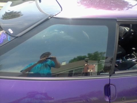 1995 Ford Probe - A reflection in the window of a purple 1995 Ford Probe shows the owner taking a photo with a phone. A cartoon bear sticker and the word "PR…