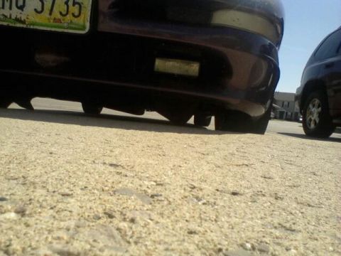 1995 Ford Probe - Low angle shot of the rear bumper and tires of a dark colored car, possibly a Ford Probe, parked on a gravel surface. A portion of a licens…