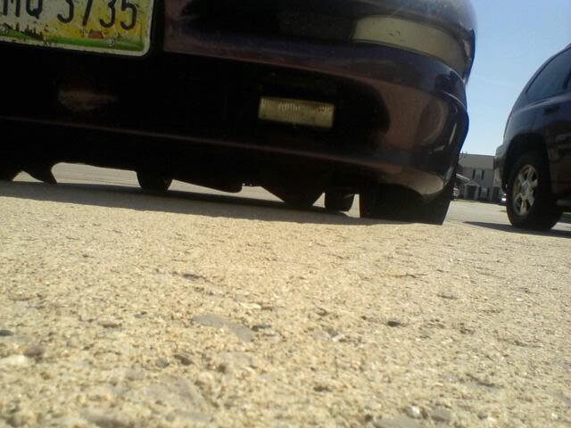 Rear bumper and tires of a dark car on gravel, with partial license plate "MQ 3735".