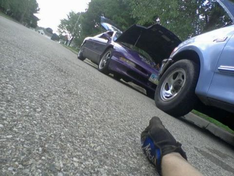 1995 Ford Probe - A low-angle shot shows the front of a light blue pickup truck parked next to a dark purple coupe with its hood open. A gloved hand is visib…