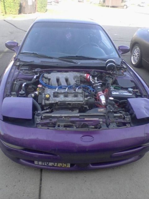 1995 Ford Probe - The front view of a modified purple 1995 Ford Probe with the hood open, revealing the engine bay and turbocharger setup. The car is parked…