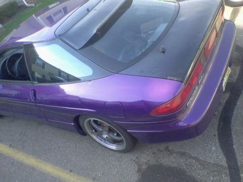 1995 Ford Probe - The rear passenger side quarter of a modified purple 1995 Ford Probe is shown from a high angle, parked on asphalt with yellow painted line…