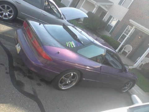 1995 Ford Probe - A purple 1995 Ford Probe is parked on asphalt with a silver sedan in the background. The car has a black hood and a sticker on the rear win…
