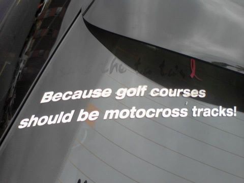 1995 Ford Probe - White text on the rear window of a car reads "Because golf courses should be motocross tracks!". A pink ribbon decal is also visible.