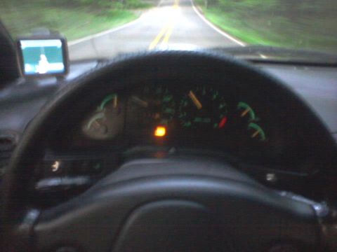 1995 Ford Probe - Interior view of a car looking through the steering wheel at the dashboard gauges and a GPS unit mounted on the windshield. The road and tr…