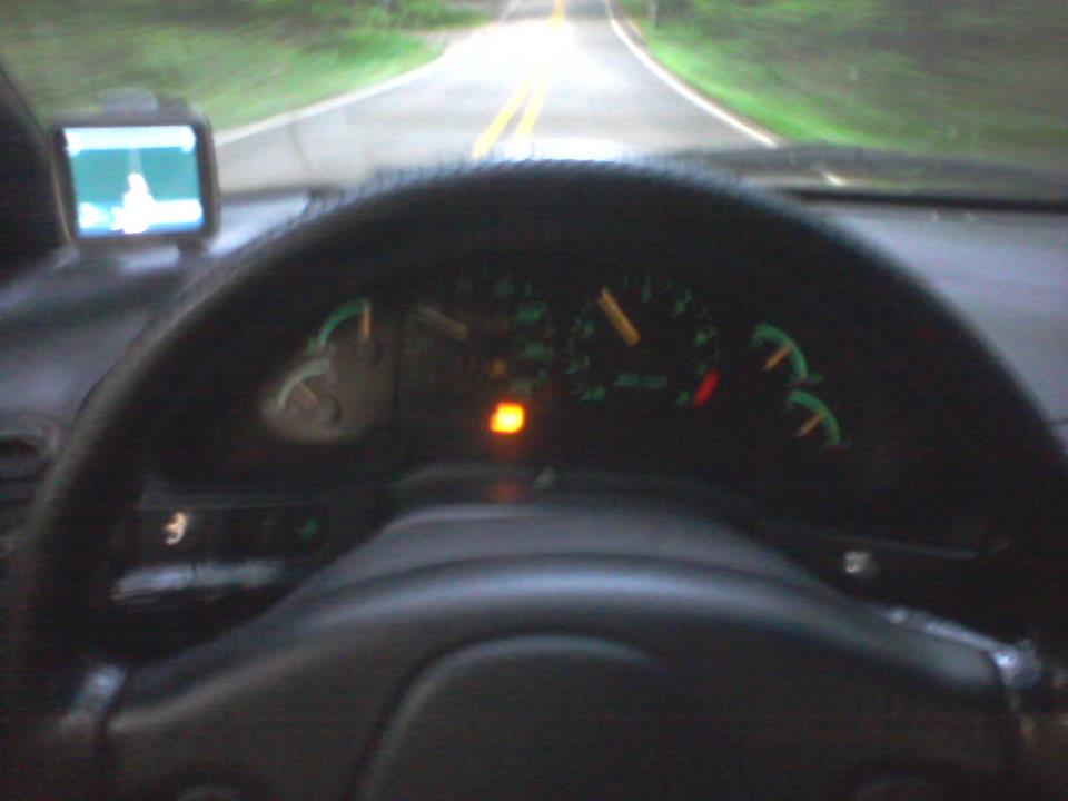 Car interior showing dashboard, steering wheel, GPS, and road through windshield.