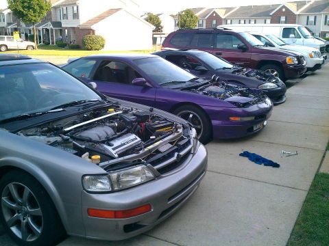 1995 Ford Probe - A line of cars with hoods open, parked on a paved surface in front of residential buildings. The closest vehicle is a silver sedan, followe…