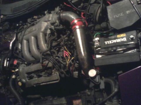 1995 Ford Probe - The image shows a close-up view of a car engine bay, featuring a Duracell car battery and a fuse box. A prominent silver intake pipe with r…