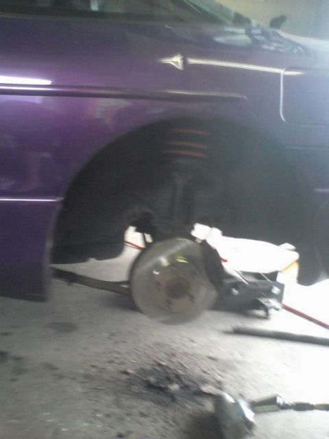 1995 Ford Probe - A close-up, low-angle shot of the front passenger-side wheel well of a purple car, showing the brake rotor and suspension components. The v…