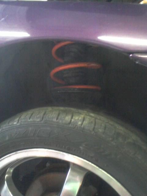 1995 Ford Probe - A close-up view of the rear wheel well of a purple vehicle, showing an orange coil spring and a tire with silver alloy rims.