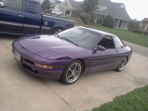 1995 Ford Probe - A purple 1995 Ford Probe is parked on a concrete driveway next to a dark blue pickup truck. The car is viewed from a three-quarter front an…