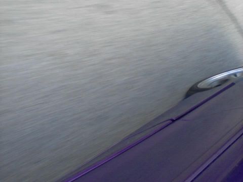 1995 Ford Probe - The side of a purple vehicle is visible, with a blurred gray background suggesting motion. A chrome door handle is also visible.