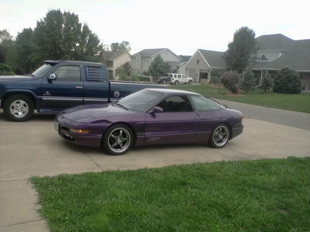 Purple 1995 Ford Probe GT parked on driveway next to blue pickup truck.