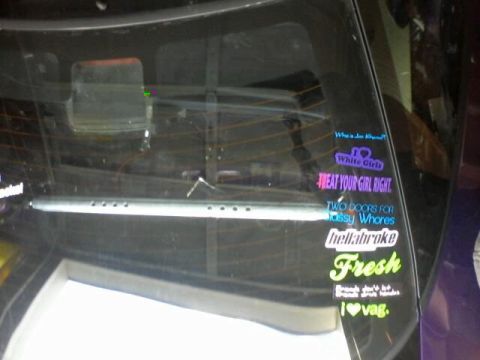 1995 Ford Probe - The rear window of a car with multiple colorful stickers applied to the glass. Visible stickers include text like "White Girls", "TREAT YOU…